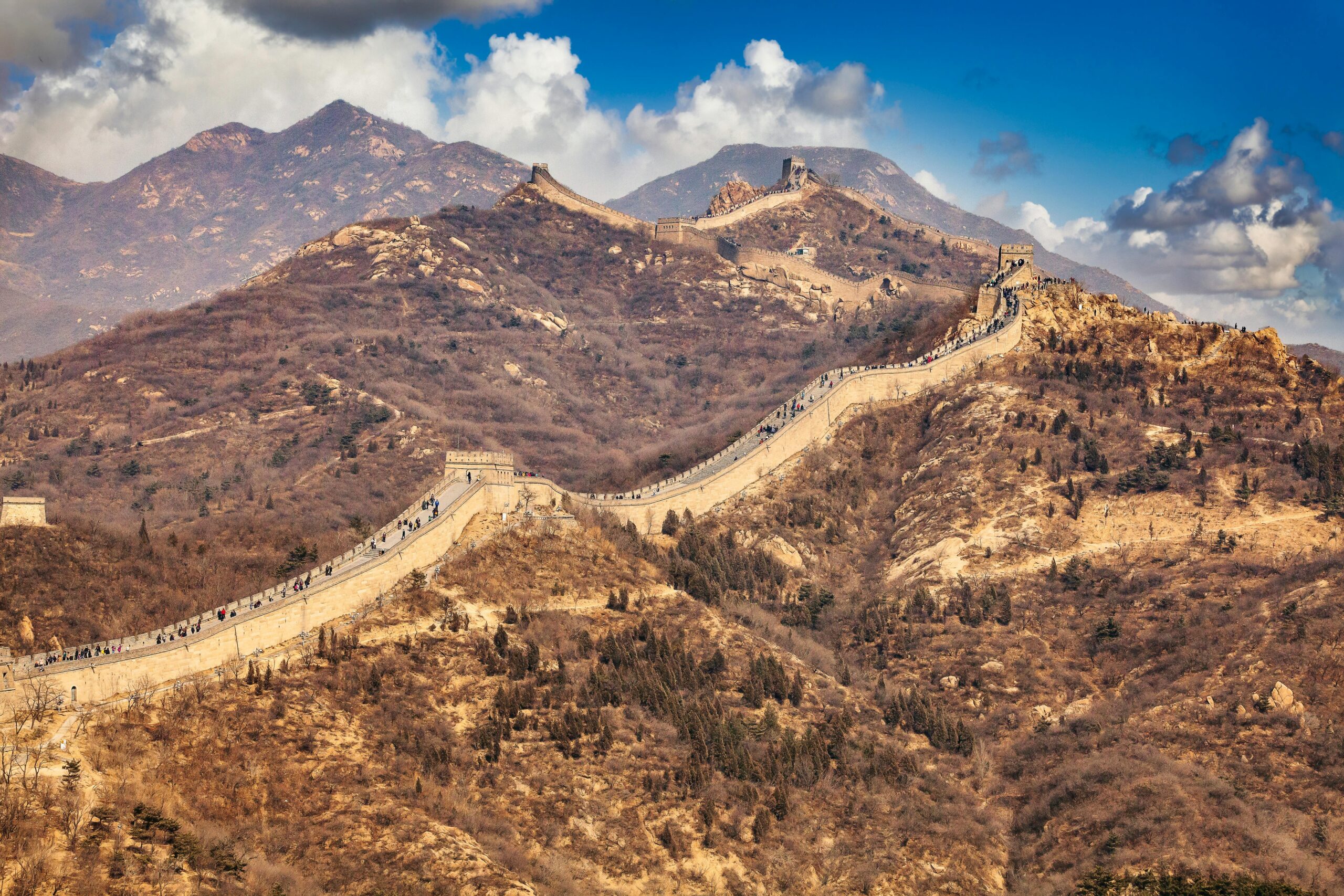 Scenic view of the Great Wall weaving through the mountainous terrain under a blue sky.