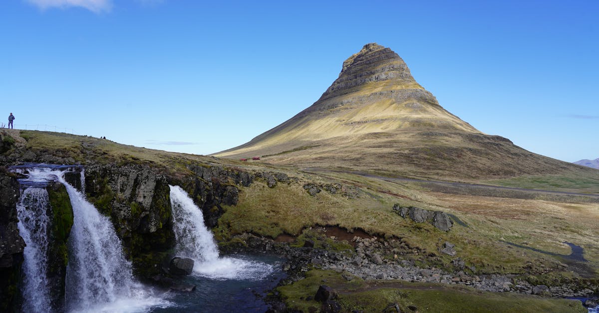 A stunning view of Kirkjufell Mountain with nearby waterfall under a clear blue sky in Iceland.